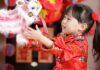 A young girl in traditional Chinese attire smiling and playing with a festive lion dance puppet during Lunar New Year celebrations.