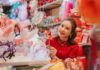 Young woman in traditional attire exploring a festive market decorated with colorful ornaments and Lunar New Year decorations.