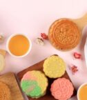 Assorted colorful mooncakes with cups of tea, celebrating the Mid-Autumn Festival.