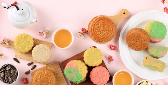 Assorted colorful mooncakes with cups of tea, celebrating the Mid-Autumn Festival.