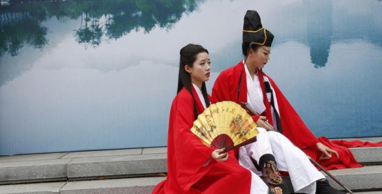 Two women dressed in traditional Chinese attire sitting by a reflective lake, symbolizing cultural appreciation.