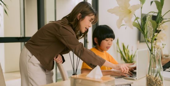 A teacher providing personalized guidance to a young student at a laptop, fostering a supportive learning environment.